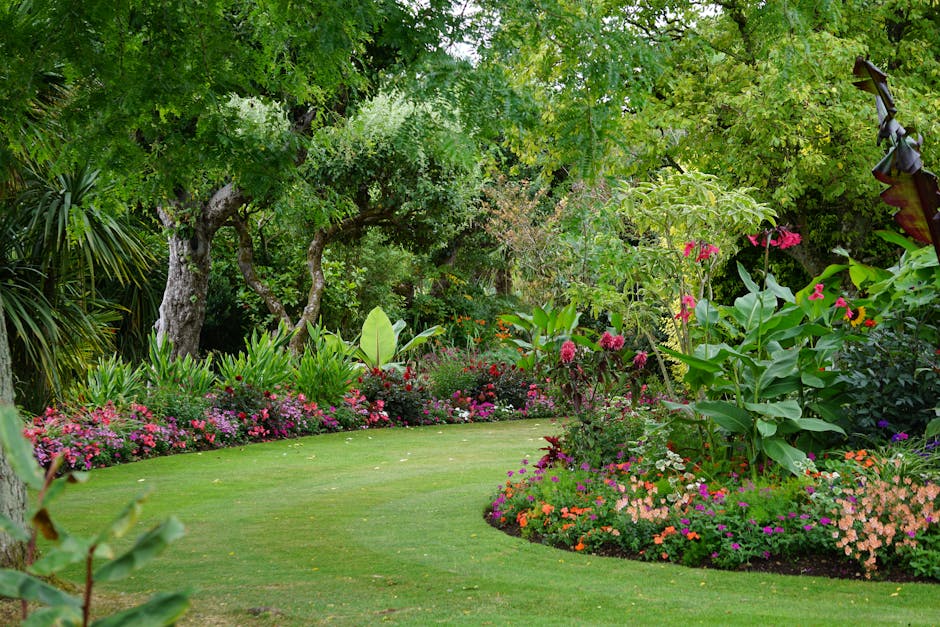 A lush garden scene showcasing a well-maintained lawn with evenly trimmed grass, bordered by vibrant flower beds filled with colorful blooms such as pink, purple, and orange flowers, along with lush g
