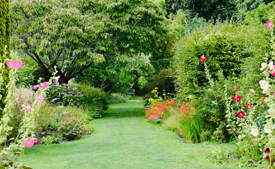 A lush garden scene showcasing a well-maintained lawn with evenly trimmed grass, bordered by vibrant flower beds filled with colorful blooms such as pink, purple, and orange flowers, along with lush g